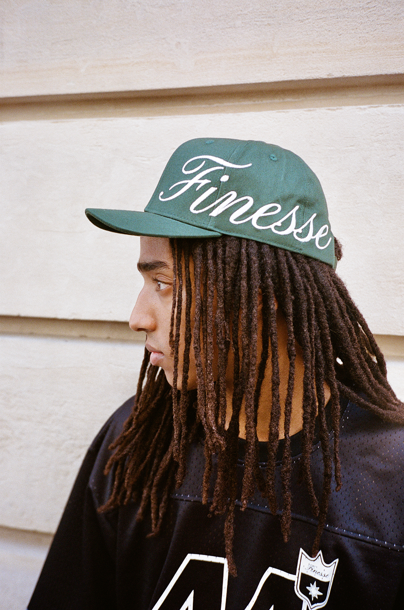 Homme portant une Finesse Sign Cap verte, regard à droite devant un mur.