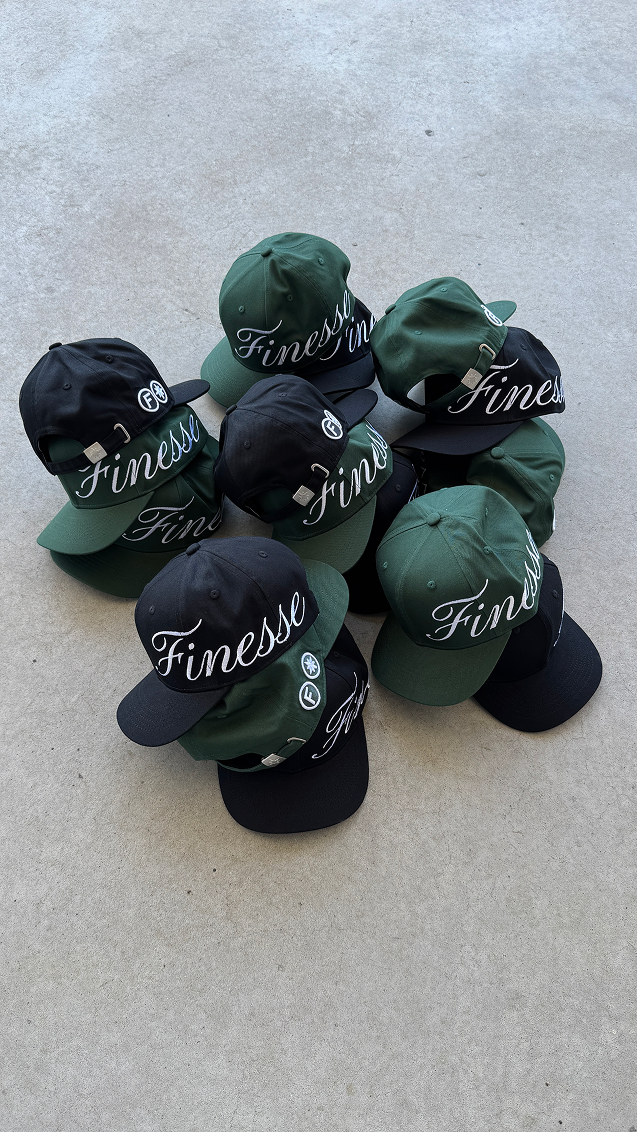 Plusieurs casquettes Finesse Sign Cap noires et vertes posées au sol en packshot.