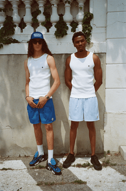 Deux hommes en Swim Shorts et Tank Top, même scène urbaine sous un angle différent.