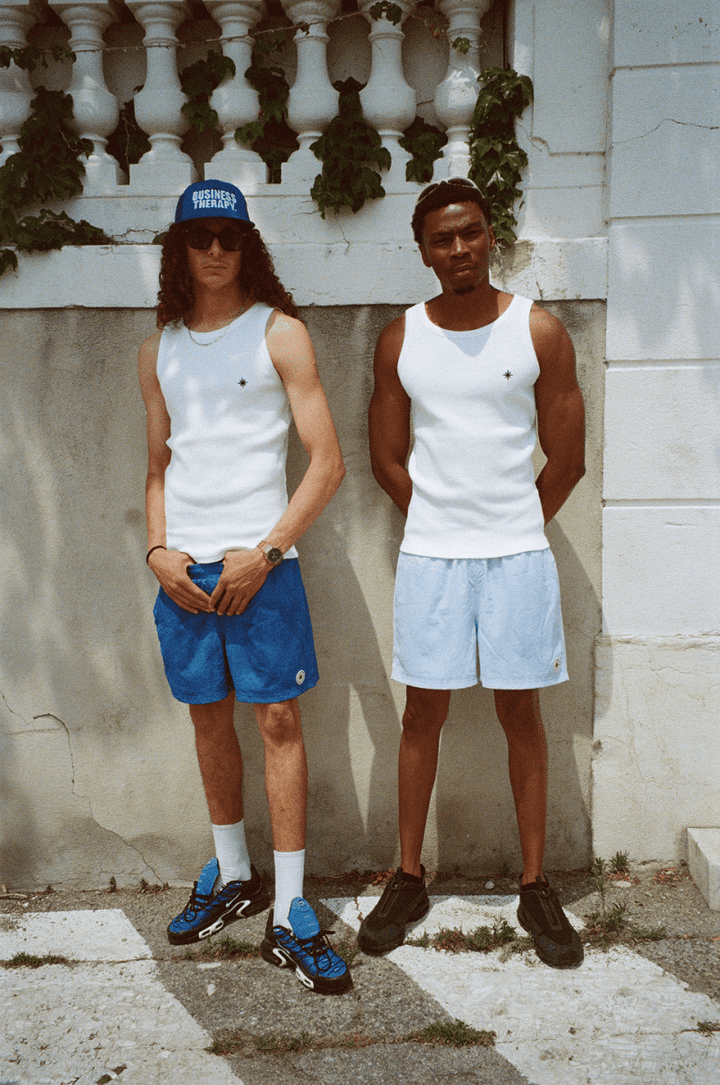 Deux hommes en Swim Shorts et Tank Top, même scène urbaine sous un angle différent.